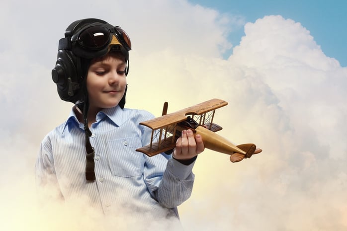 Image of little boy in pilots helmet playing with toy airplane against clouds background.jpeg